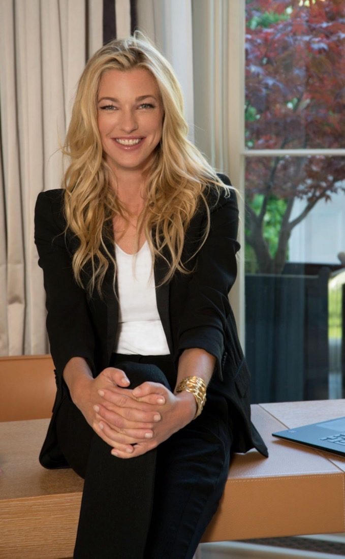 Nicole Junkerman with a warm, welcoming smile, seated at a desk by a window