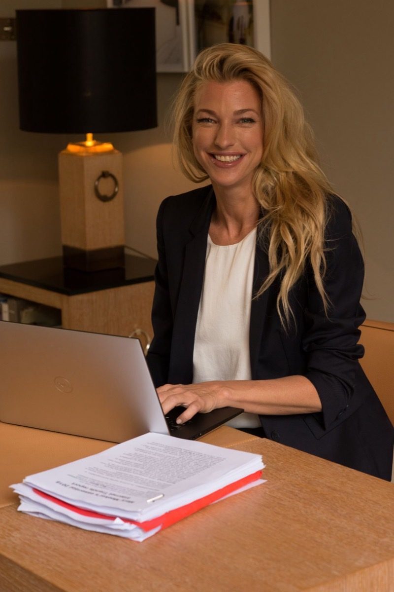 Nicole Junkerman writing at a lamp-lit desk with a warm smile, a notebook and laptop to hand