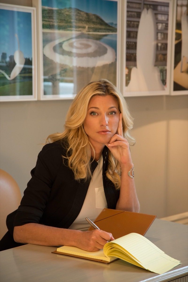 Nicole Junkerman writing notes in a notebook at a desk, thoughtful, with framed prints behind